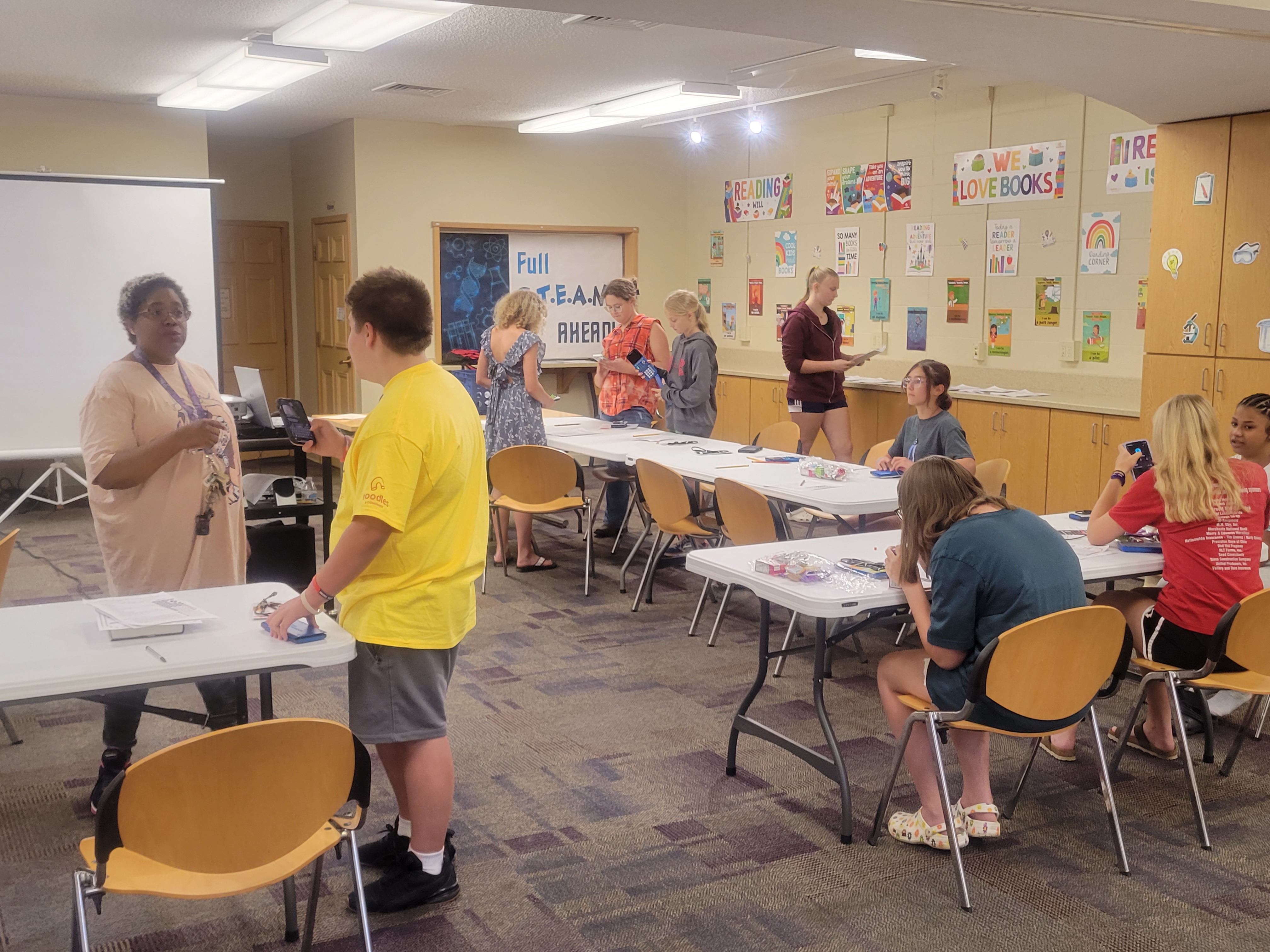 teens standing/sitting around tables with a teacher instructing them on how to use graphing calculators